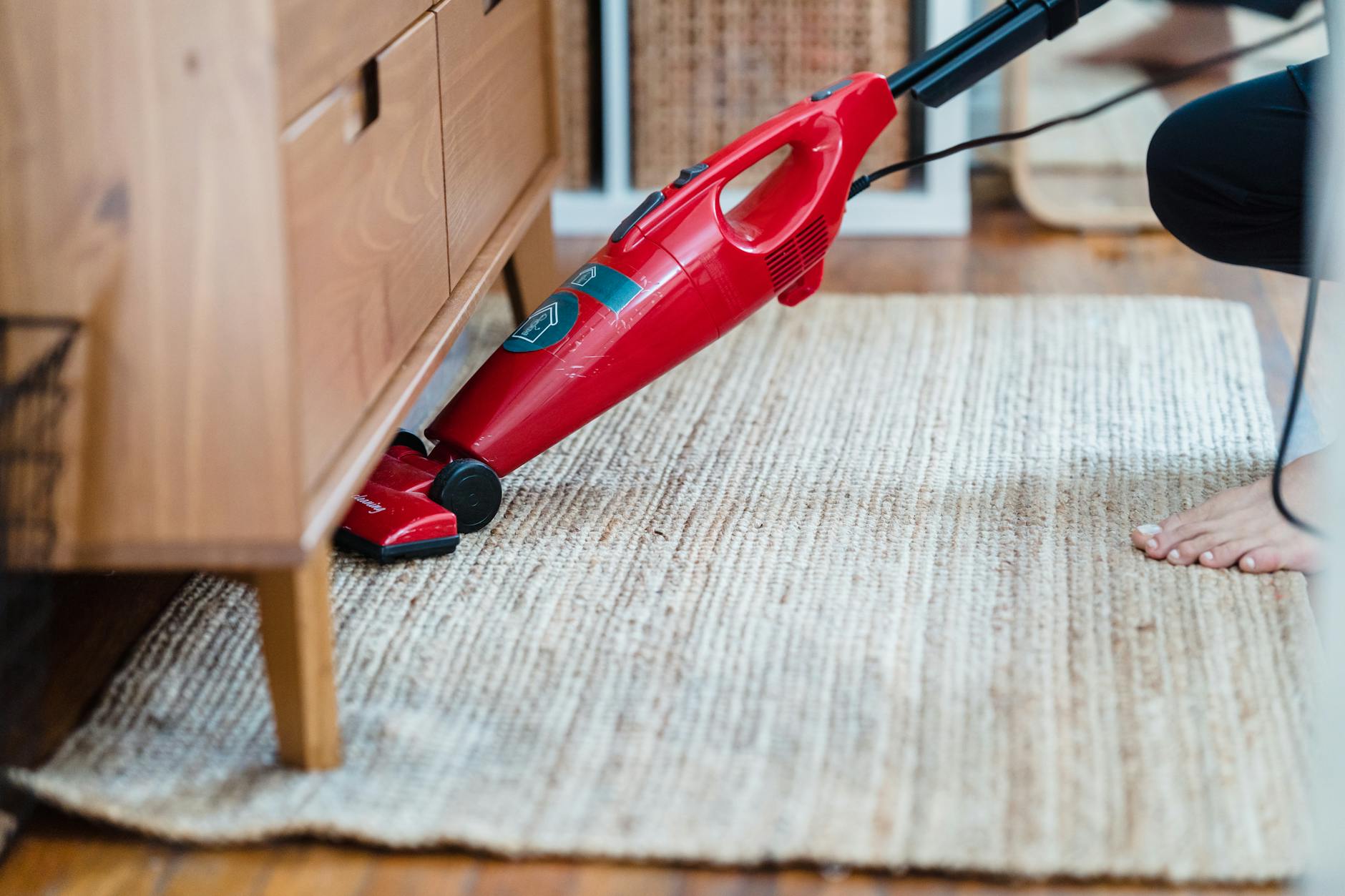 Vacuuming Carpet Thoroughly Before and After Stain Treatment Person using a vacuum cleaner under furniture on a rug — thorough vacuuming is a key step in carpet stain prevention and preparation