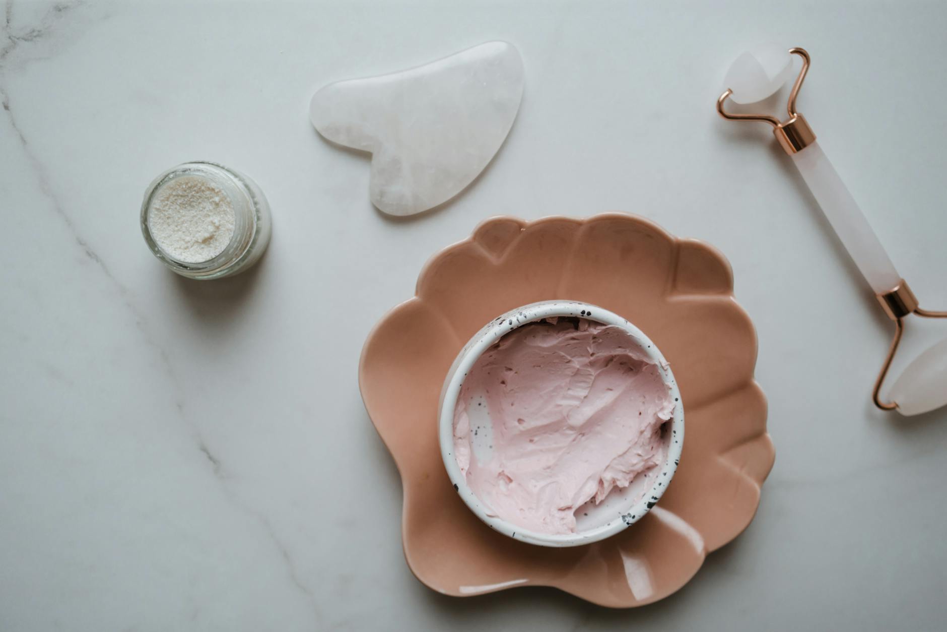 Anti-Aging Skincare Products Flat Lay Skincare essentials including cream, gua sha stone, and facial roller arranged on a marble surface