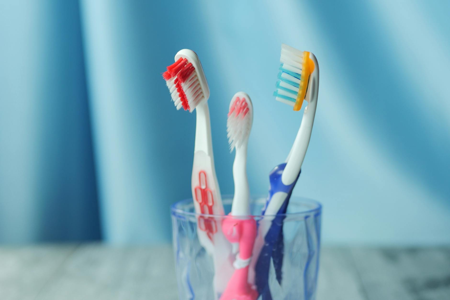 Toothbrushes Stored Together in a Glass Multiple colorful toothbrushes stored together in a glass — a common source of cross-contamination