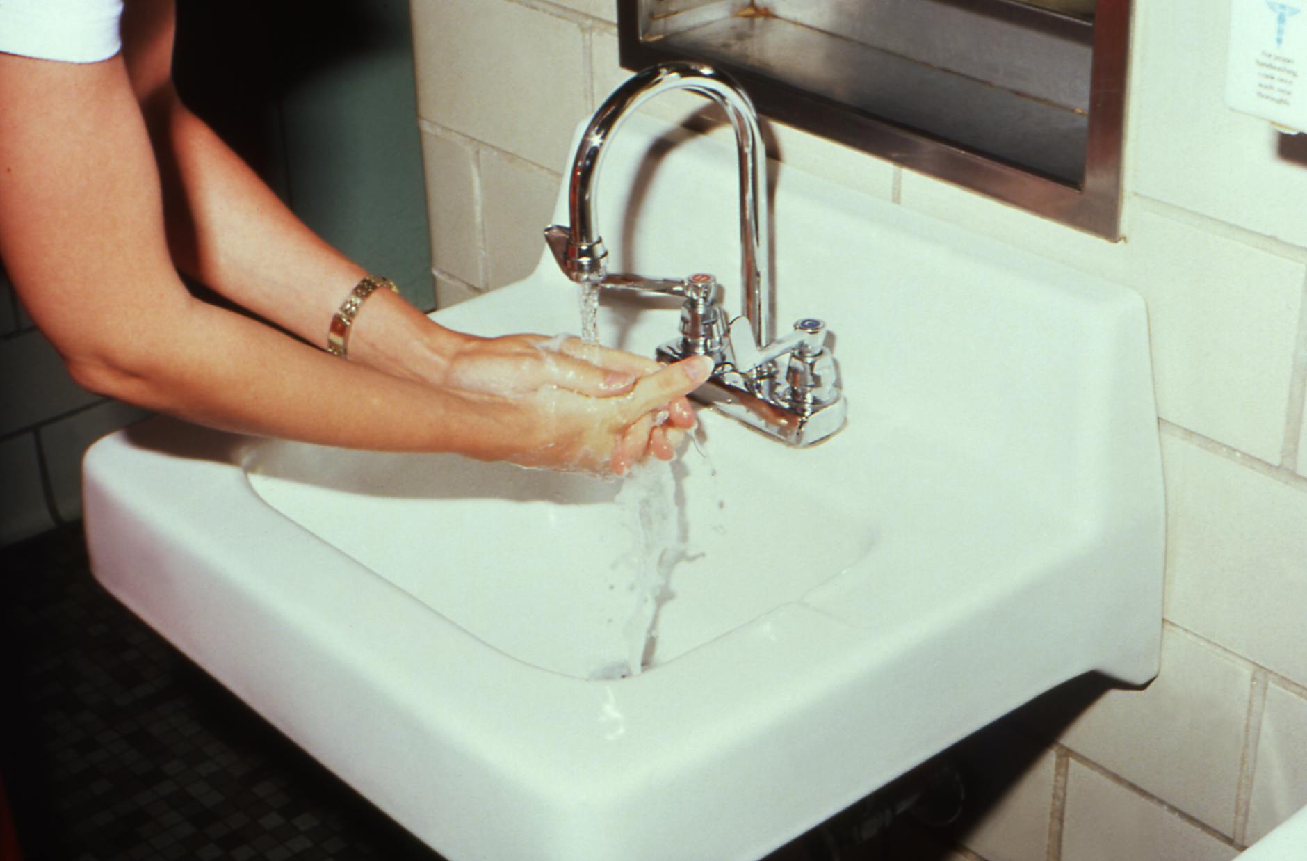 Proper Hand Washing Before Brushing Reduces Toothbrush Contamination Woman washing hands at bathroom sink to prevent cross-contamination and spread of bacteria
