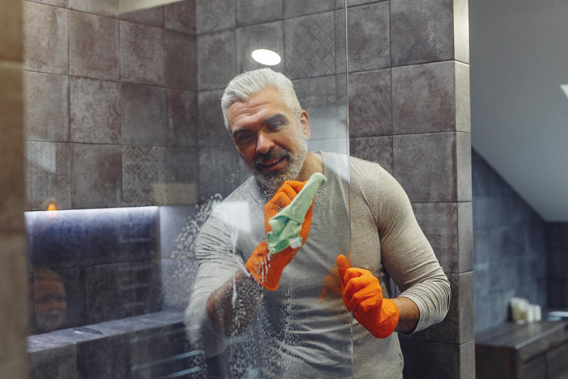 Bathroom Cleaning Hacks - Squeegee Shower Glass Man wearing rubber gloves cleaning a shower glass panel