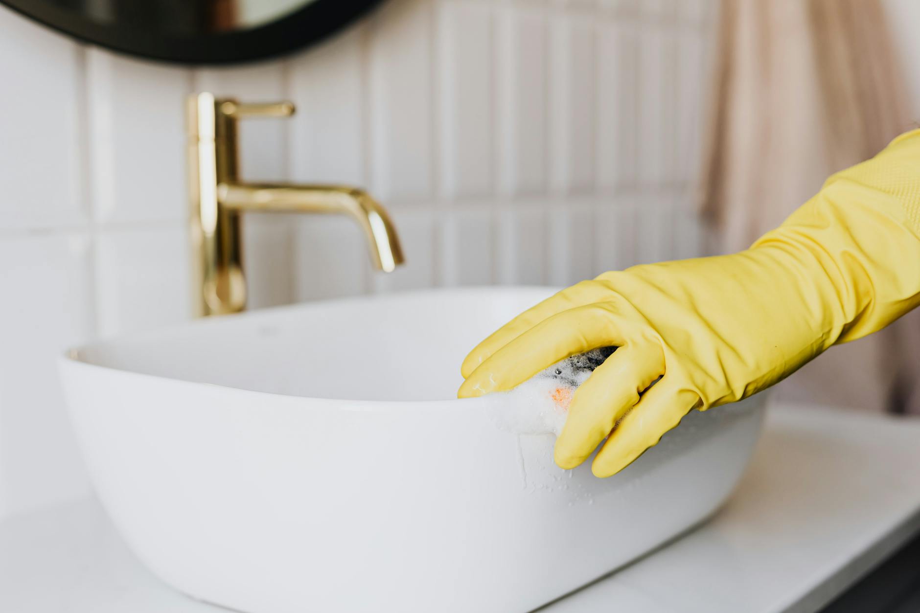 Bathroom Sink Cleaning Tips Person in yellow rubber gloves cleaning a white bathroom sink