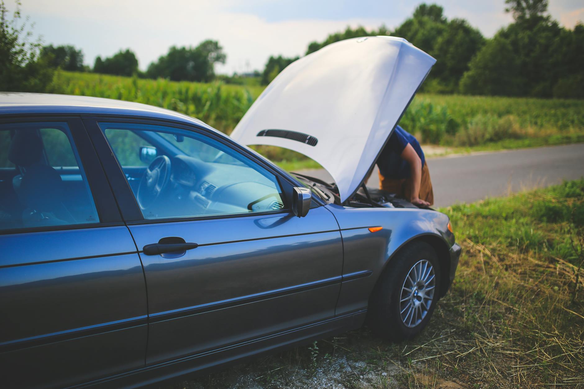 Roadside Car Breakdown - Car Emergency Kit Checklist 2026 Man checking car engine with hood open by the side of a rural road