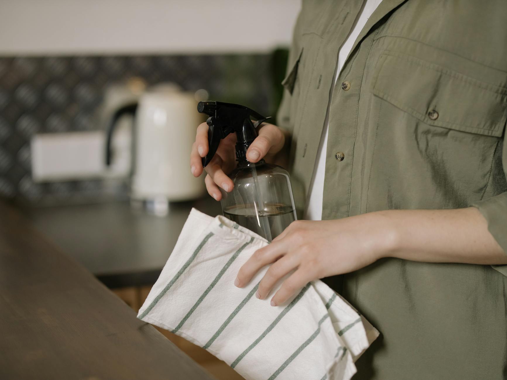 Proper Surface Cleaning Technique in the Kitchen A person spraying and wiping a kitchen counter with a cloth, demonstrating proper technique