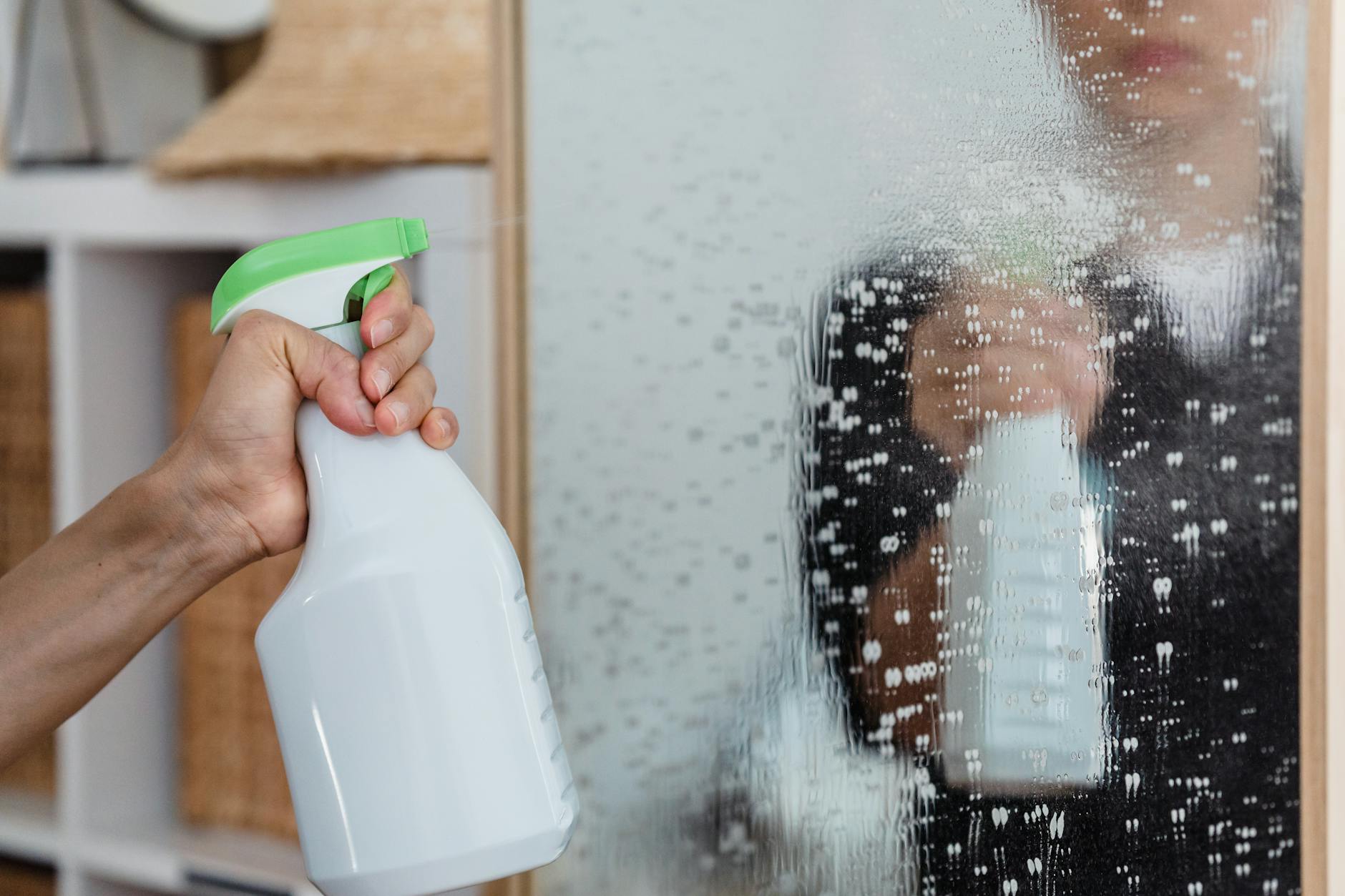 Using Too Much Cleaning Product — Common Cleaning Mistake Hand using spray bottle to clean a mirror — using too much product is a common cleaning mistake