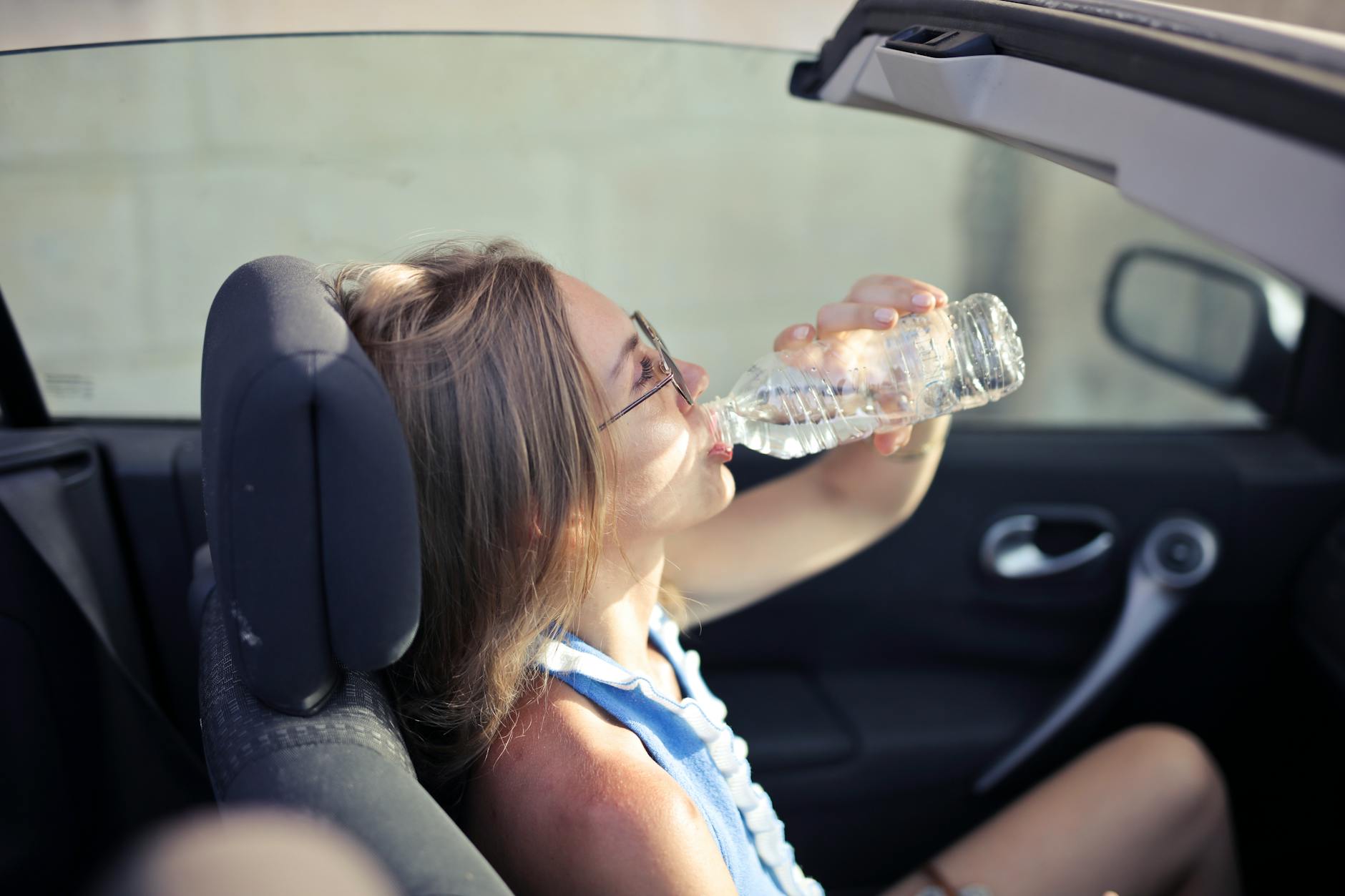 Unsecured drinks in vehicles contribute to distracted driving risk Woman drinking from a water bottle while seated in a car — illustrating the distraction risk of unsecured drinks