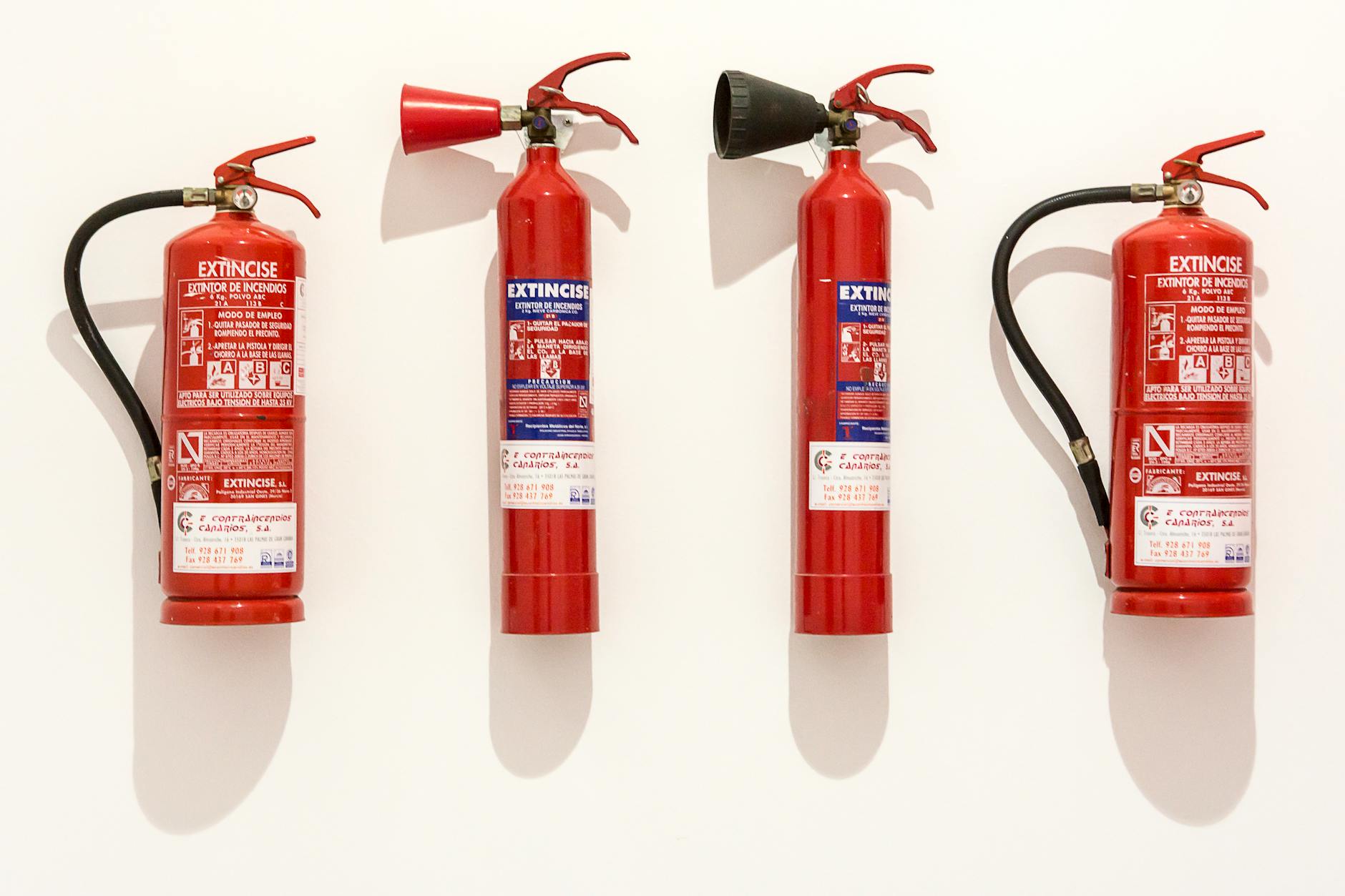 Fire Extinguisher Types for Home — Proper Wall Mounting Four red fire extinguishers mounted on a white wall showing proper storage and placement