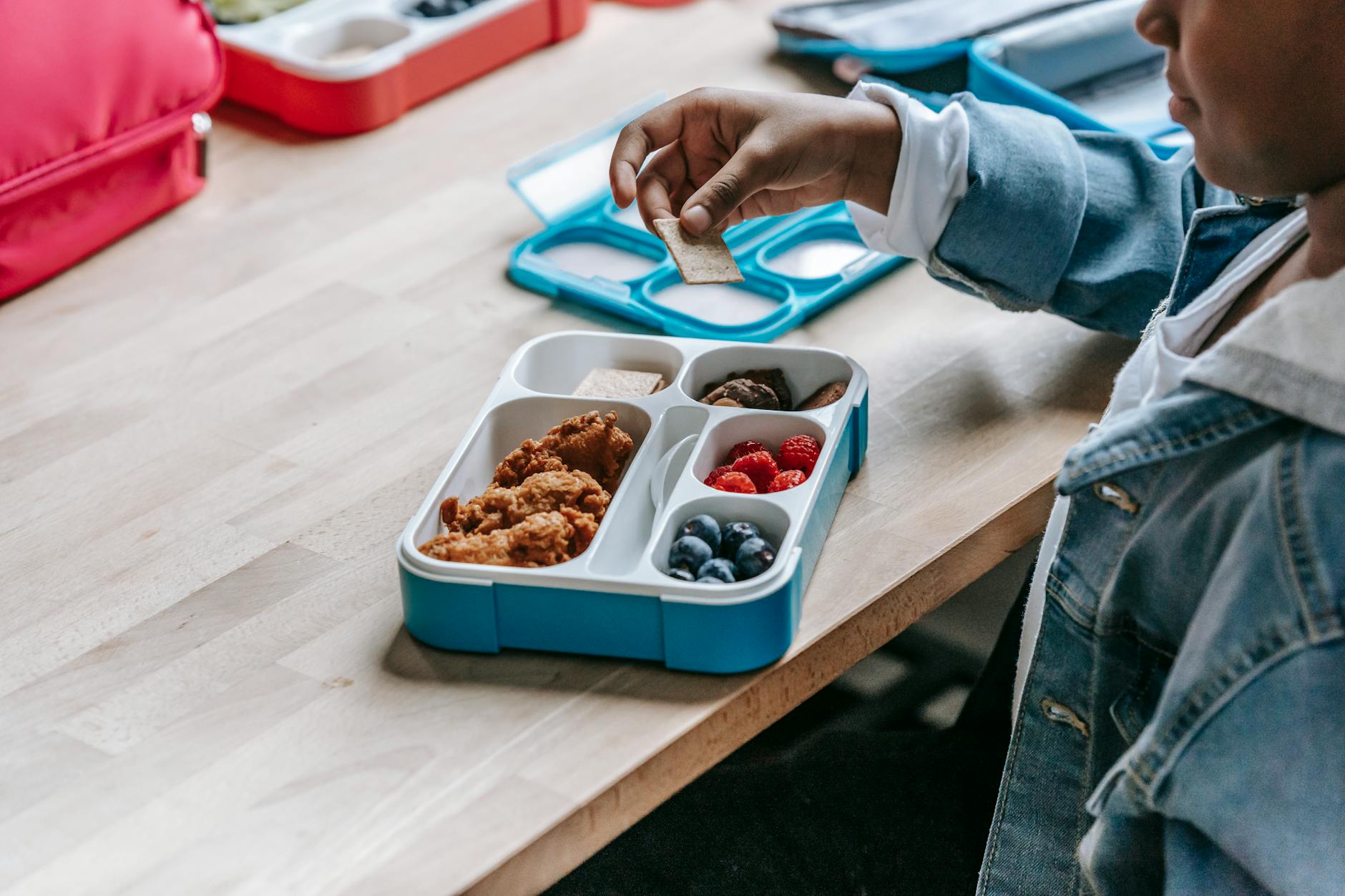 Healthy School Lunchbox Ideas for Kids 2026 School-age child at a table with a healthy packed lunch container and drink