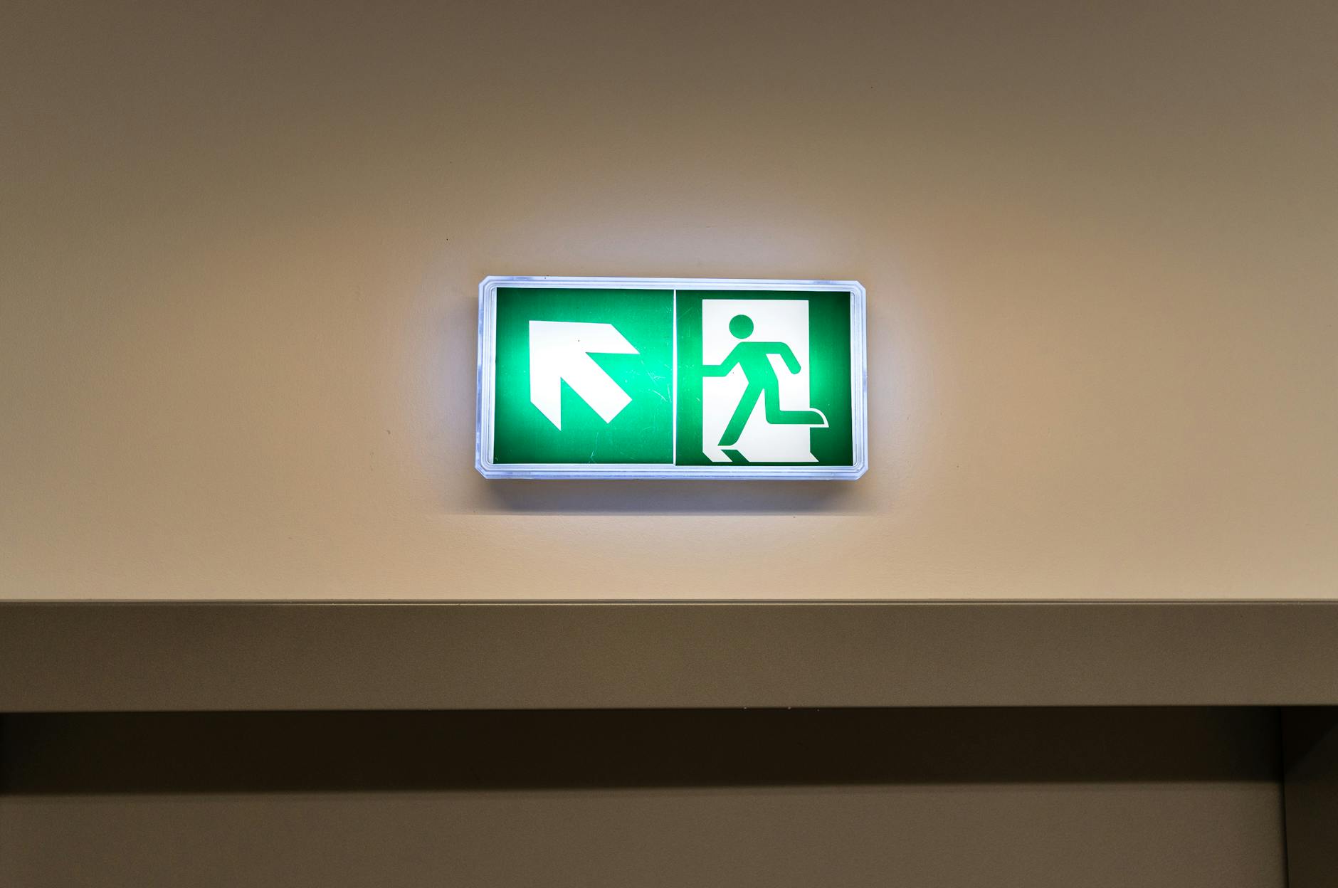 Emergency Exit Sign — Fire Escape Route Indicator Bright green emergency exit sign with directional arrow in an indoor hallway — a key element of any fire escape route
