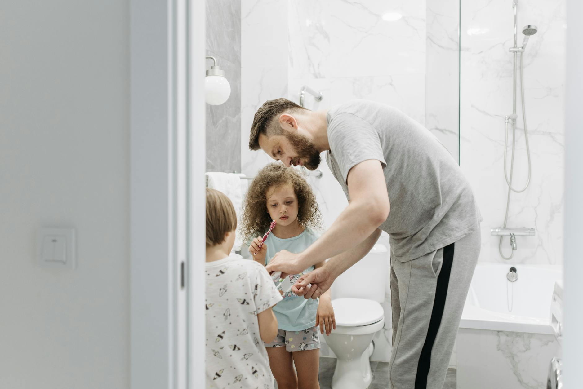 Family Bathroom Hygiene Daily Routine 2026 Father and children in a bathroom during their daily hygiene routine, illustrating high-traffic household bathroom use