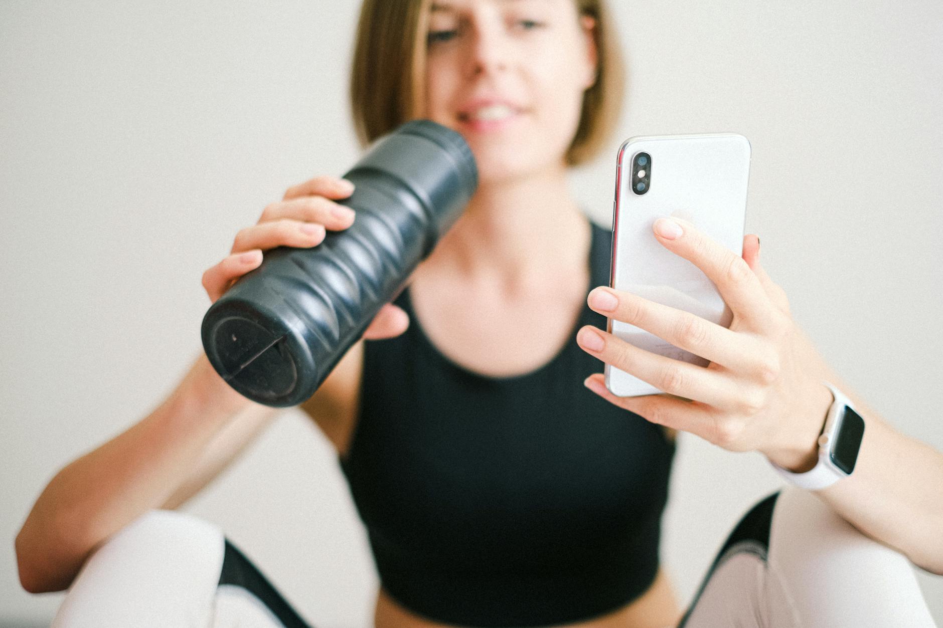 Checking Phone Battery During Workout Woman checking smartphone while resting during a home workout with a sports bottle