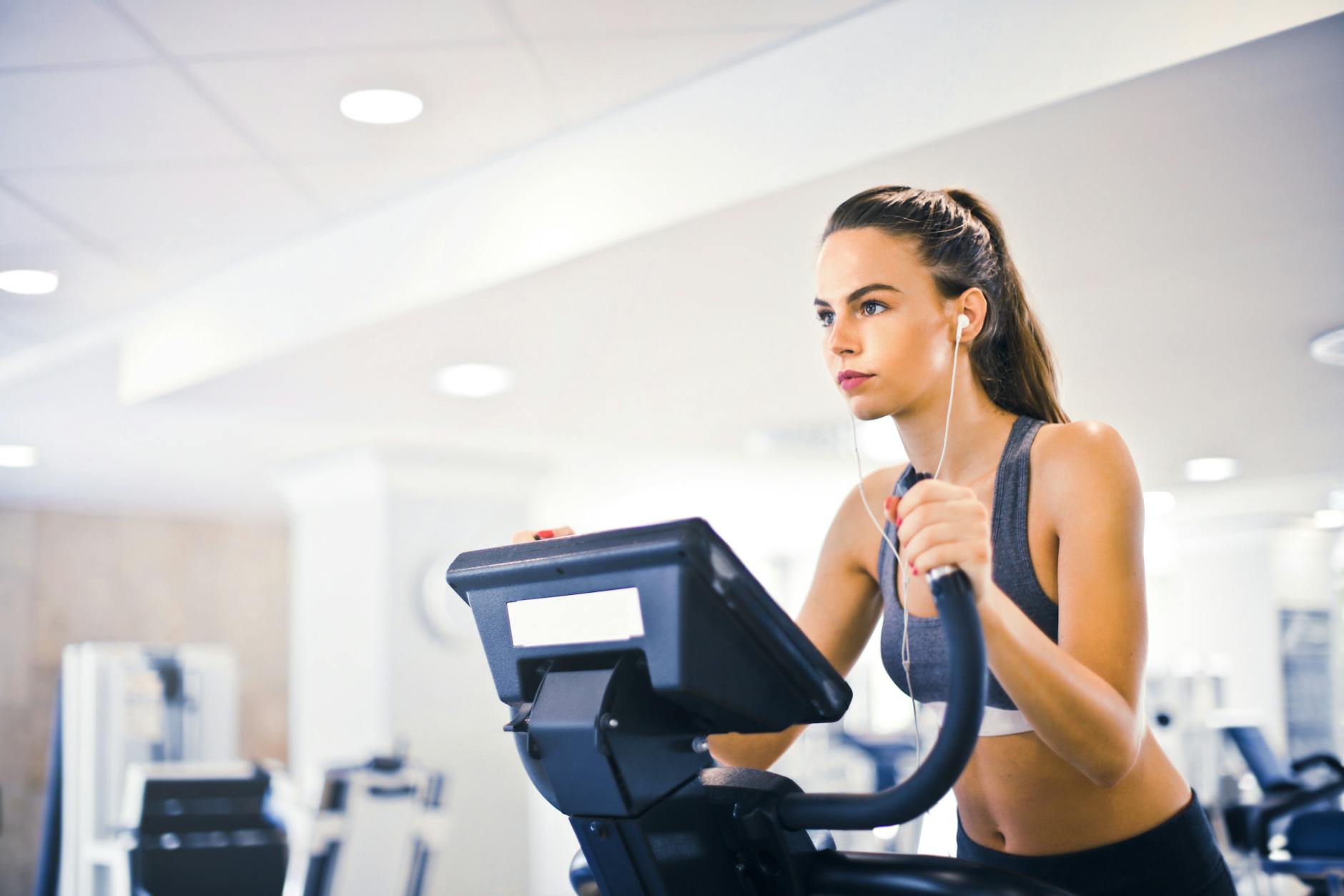 Running on Treadmill with Phone and Earphones at Gym Woman running on treadmill wearing earphones and streaming music on her phone at the gym