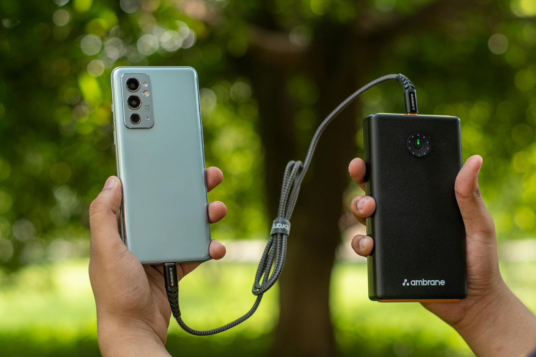 Portable Phone Charger Power Bank for Sports Events 2026 Hands holding a smartphone connected to a portable power bank charger outdoors