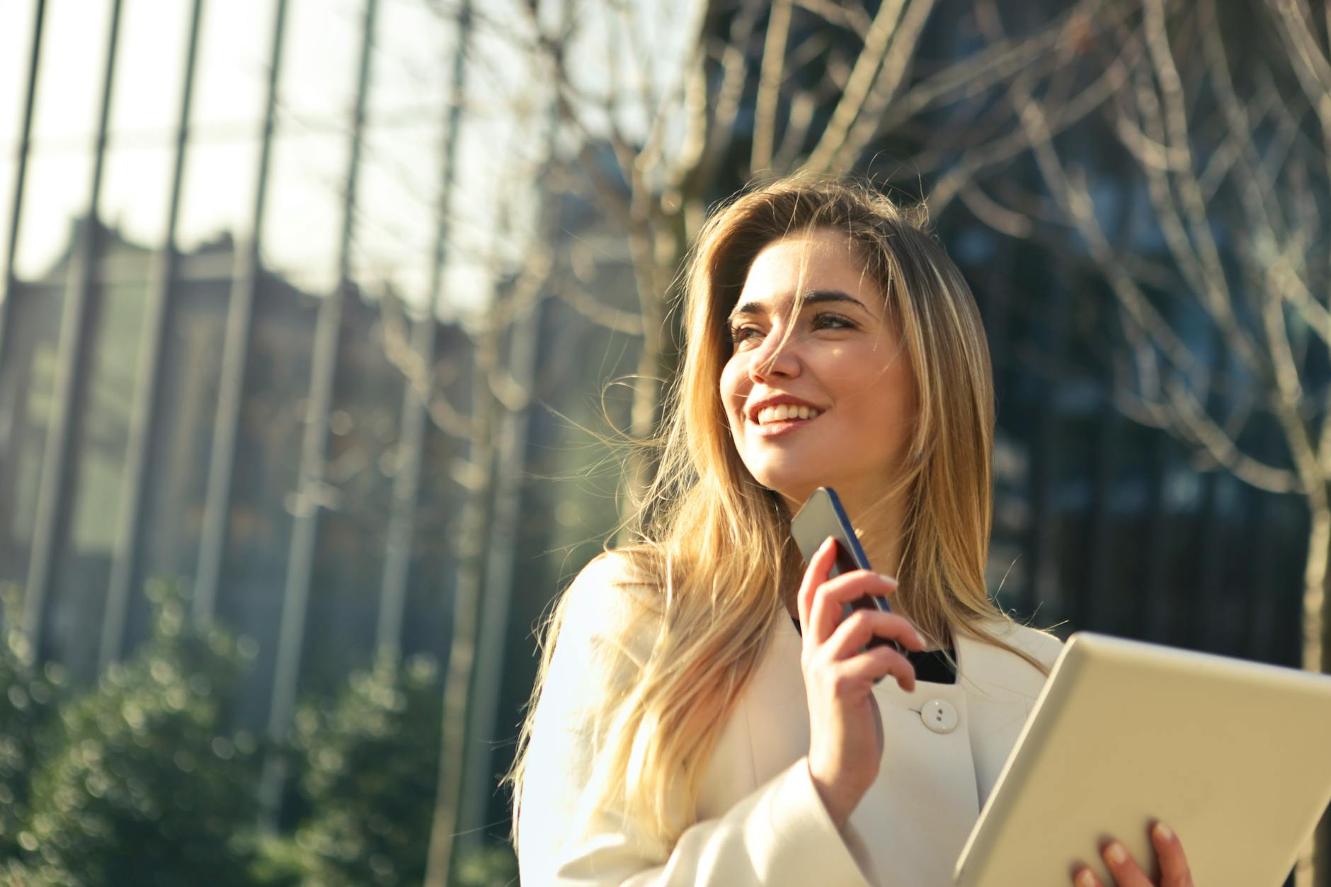 Social Confidence and Smile Self-Esteem in Professional Settings Confident businesswoman smiling outdoors while holding her phone and tablet, representing how smile confidence psychology plays out in daily professional life