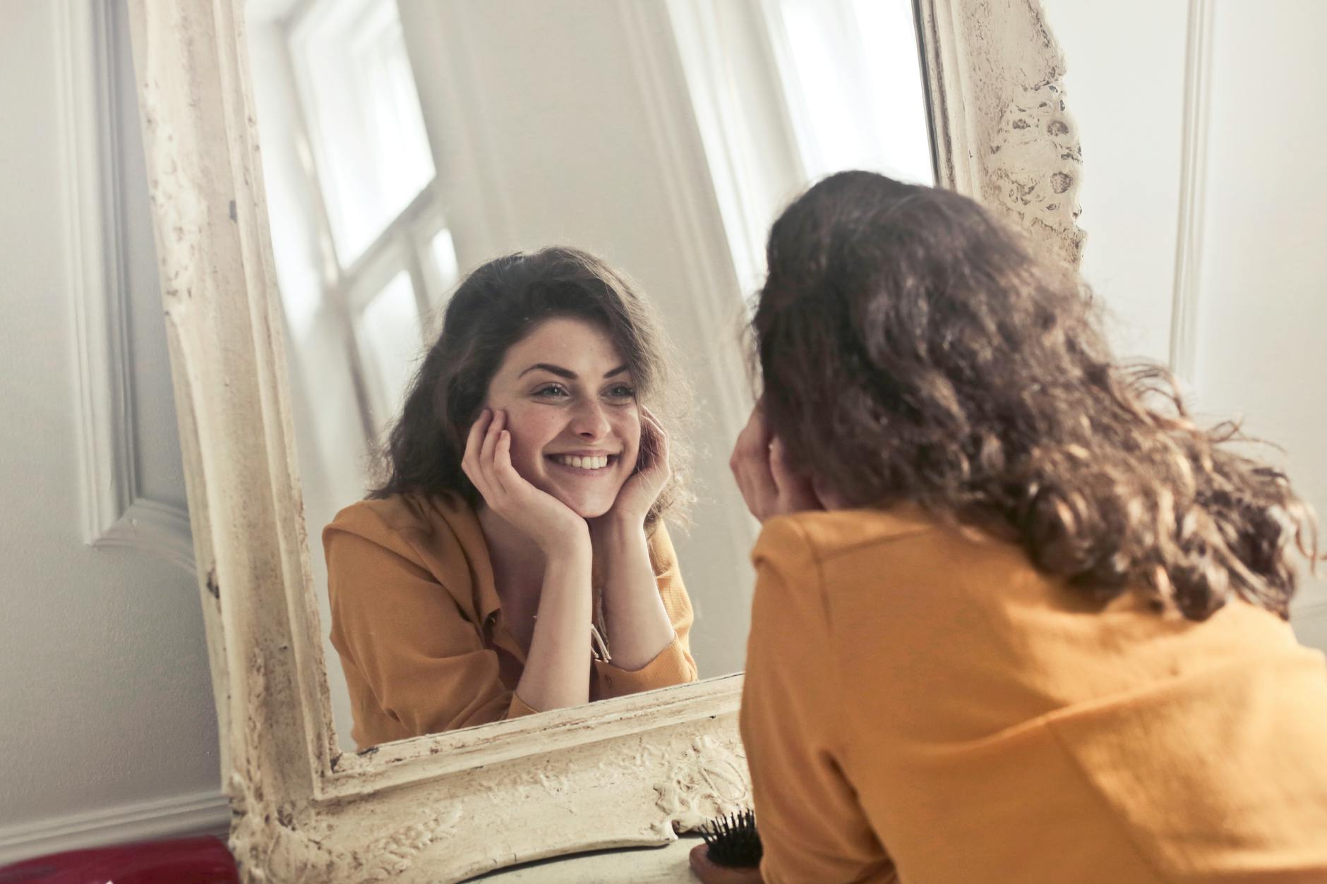 Smile and Self-Esteem — The Facial Feedback Loop Woman smiling at her own reflection in a mirror, illustrating the self-perception loop of smile confidence psychology