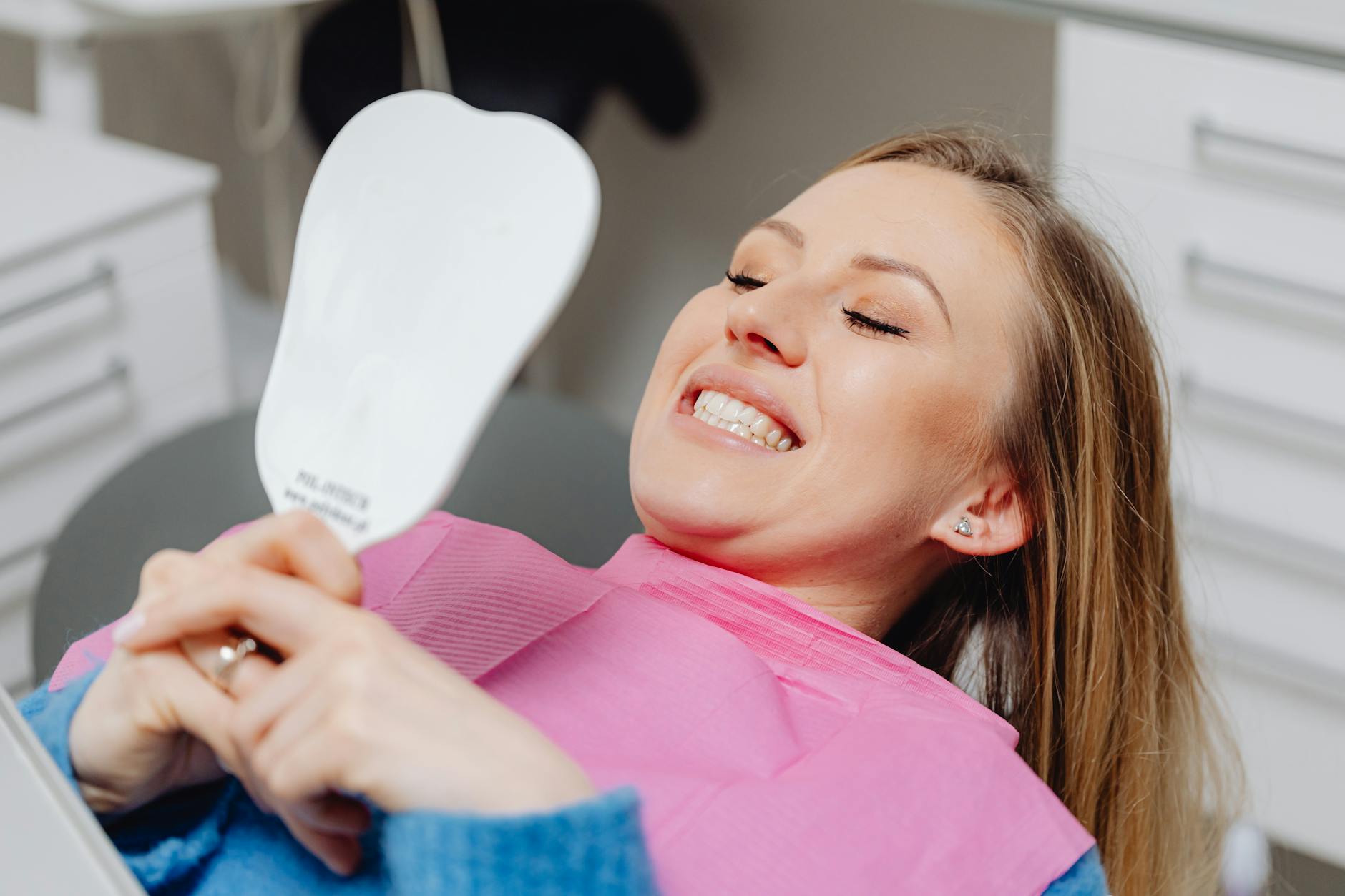 Woman Reviewing Cosmetic Dental Results Woman reviewing her smile results in a mirror at a dental clinic