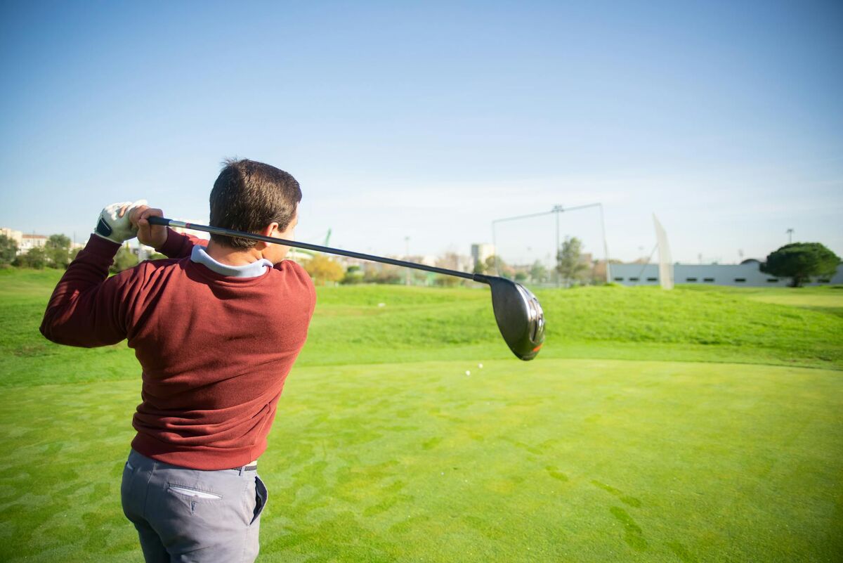 Senior Golfer Equipment and Swing Optimization Golfer in red sweater swinging on a sunny golf course