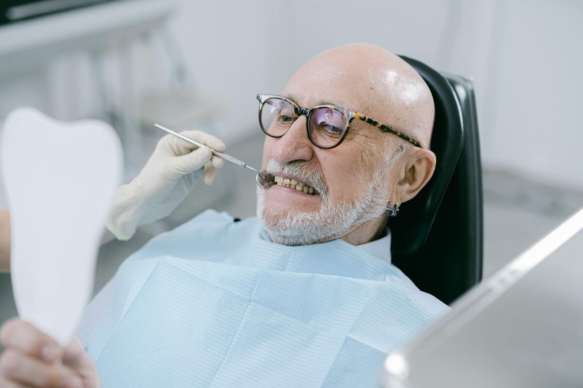Aging Teeth Yellowing Causes - Dental Examination Elderly man examining his teeth with a dental mirror during a checkup