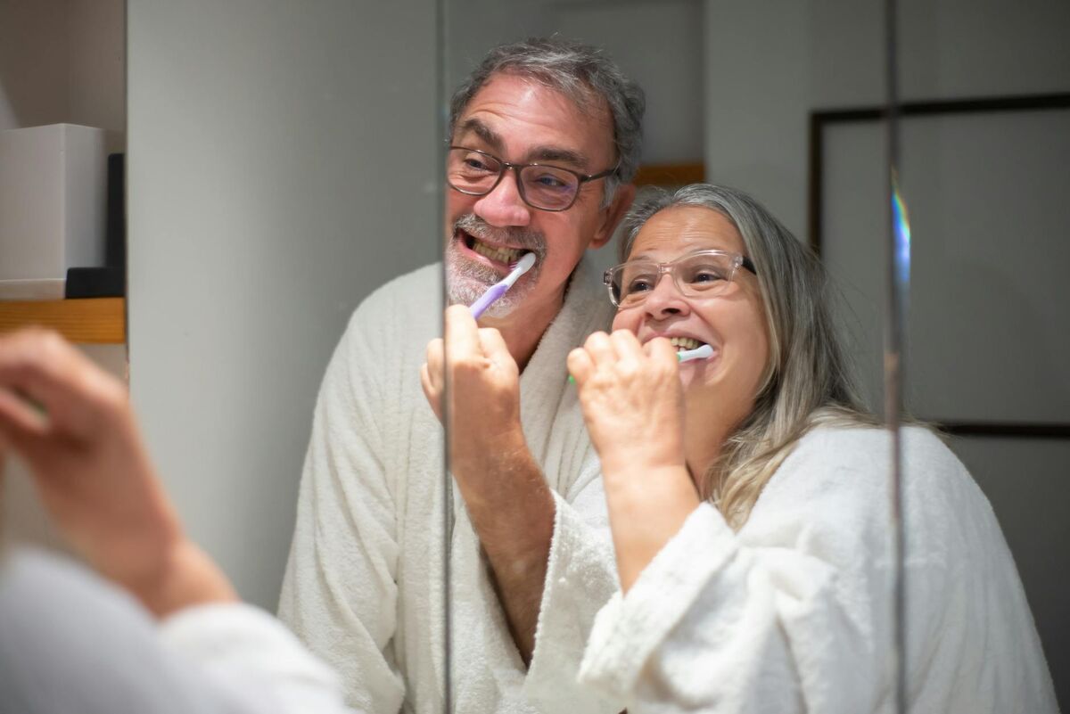Senior Dental Care - Daily Brushing Habits for Aging Teeth Senior couple brushing their teeth together in front of a bathroom mirror